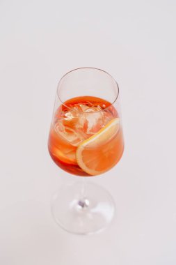 glass of aperol spritz cocktail with ice and orange on white table 