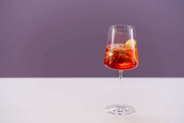 glass of aperol spritz cocktail with ice and orange on light background