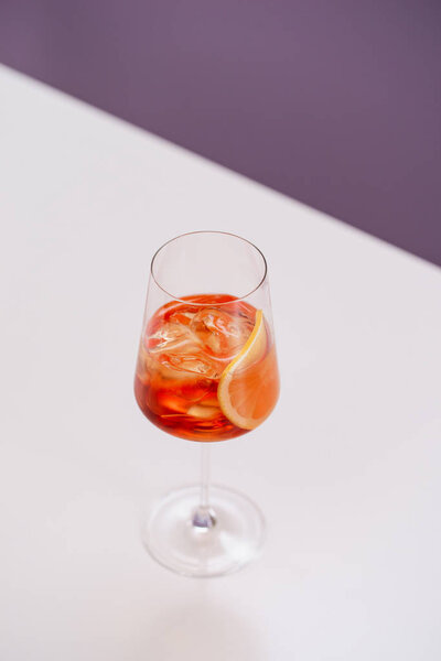 glass of aperol spritz cocktail with ice and orange on white table 