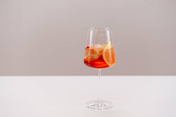 glass of aperol spritz cocktail with ice and orange on light background