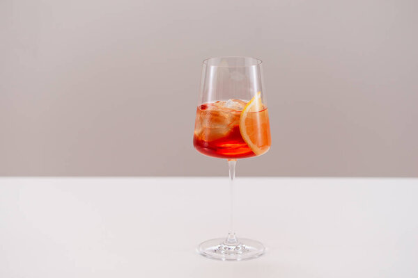 glass of aperol spritz cocktail with ice and orange on light background