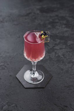 Alkol pembe kokteylinin yakın görüntüsünü gri çimento masadaki buz parçasıyla kapatın.