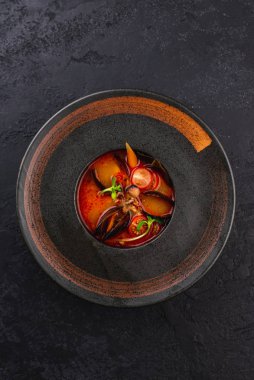 Siyah tabakta midye ve sebzeli kırmızı domates çorbası.