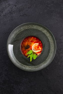 Siyah zeytinli domates çorbası ve siyah tabakta limon.