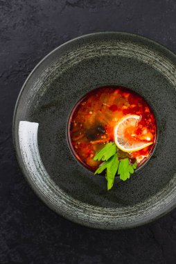 Siyah zeytinli domates çorbası ve siyah tabakta limon.