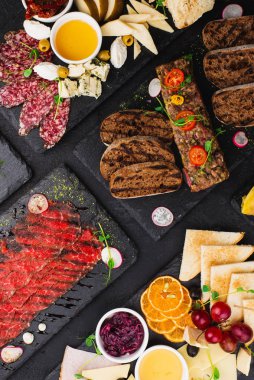 Siyah zemin üzerinde dilimlenmiş et, peynir ve ekmek parçaları seti