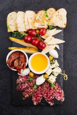 Peynir, salam ve balla dilimlenmiş ekmek ve siyah tabakta kurutulmuş domates.