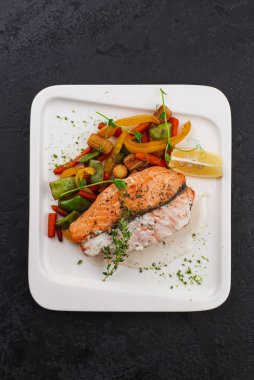 Beyaz tabakta sebzeli somon bifteği. 