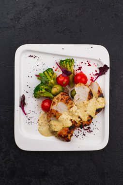 Izgara tavuk göğsü, beyaz tabakta krema sosu, brokoli ve domates ile servis edilir. 