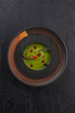 Siyah tabakta kırmızı böğürtlenli brokoli kremalı çorba.