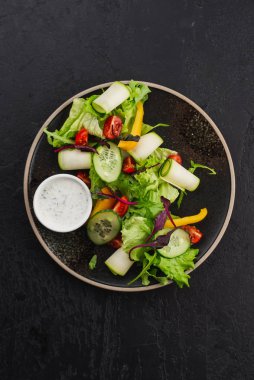 Siyah arkaplanda yoğurt soslu taze sebze salatası.