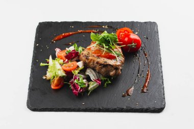 Grilled beef steak with tomatoes and salad, arugula and bbq sauce on black plate