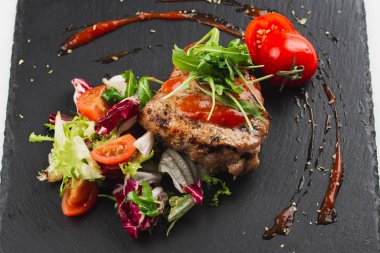 Grilled beef steak with tomatoes and salad, arugula and bbq sauce on black plate