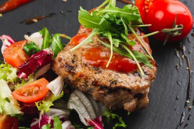 Grilled beef steak with tomatoes and salad, arugula and bbq sauce on black plate