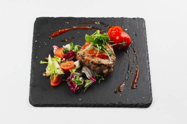 Grilled beef steak with tomatoes and salad, arugula and bbq sauce on black plate