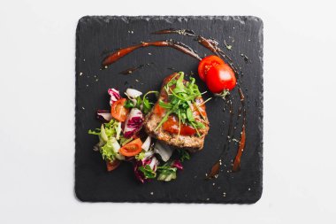 Grilled beef steak with tomatoes and salad, arugula and bbq sauce on black plate