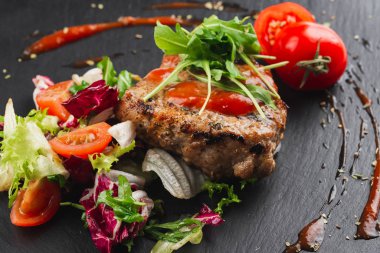 Grilled beef steak with tomatoes and salad, arugula and bbq sauce on black plate