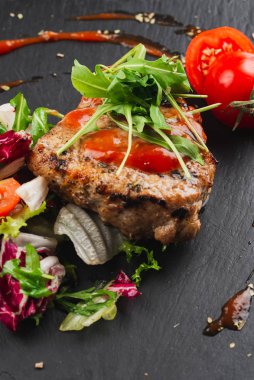 Grilled beef steak with tomatoes and salad, arugula and bbq sauce on black plate