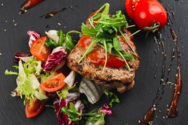 Grilled beef steak with tomatoes and salad, arugula and bbq sauce on black plate