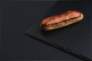 eclair with custard cream and brown chocolate glaze on black plate 