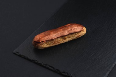 eclair with custard cream and brown chocolate glaze on black plate 