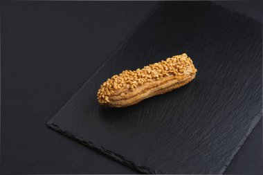 eclair with custard cream and nuts chips on black plate 