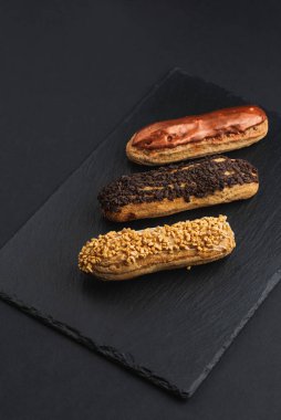 set of eclairs with custard cream and glaze on black plate 