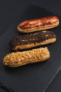 set of eclairs with custard cream and glaze on black plate 