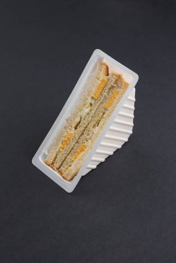 triangular white bread with cheese, eggs and mayonnaise in plastic box on the black table 