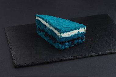 piece of blue velvet biscuit cake with white cream on black plate