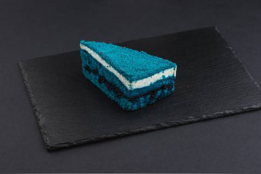 piece of blue velvet biscuit cake with white cream on black plate