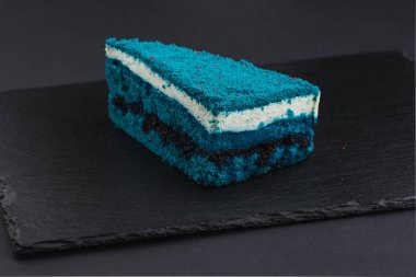 piece of blue velvet biscuit cake with white cream on black plate