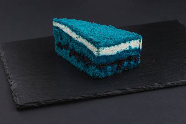 piece of blue velvet biscuit cake with white cream on black plate