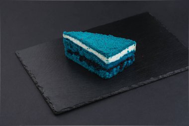 piece of blue velvet biscuit cake with white cream on black plate
