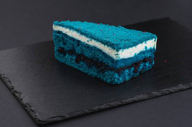 piece of blue velvet biscuit cake with white cream on black plate