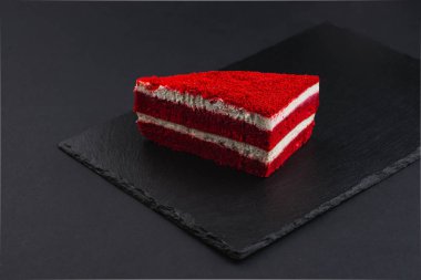 piece of biscuit red velvet cake with white cream on black plate