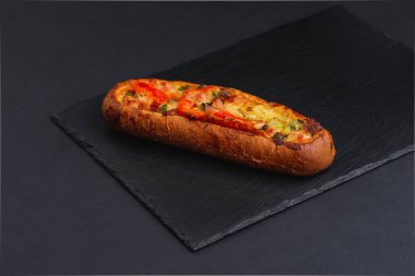 hot baked toast baguette with chopped bacon, vegetables and cheese on black plane