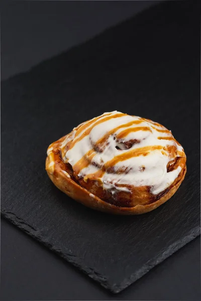 Roll Zoete Cinnabon Met Witte Room Oranje Glazuur Zwarte Plaat — Stockfoto