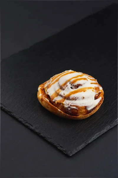 roll sweet cinnabon with white cream and orange glaze on black plate