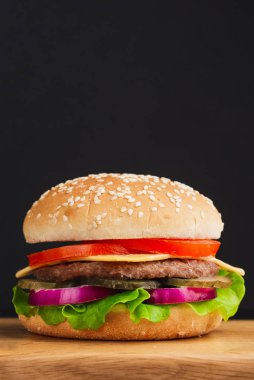  Domatesli hamburger, peynir, salatalık ve siyah arka planda marul. 