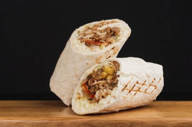 Shawarma sandviçi, siyah arka planda iki parçaya bölünmüş taze rulo.