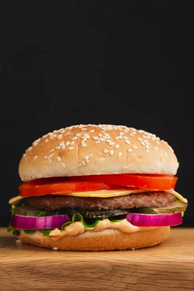hamburger with tomatoes, cheese, cucumbers and lettuce on black background