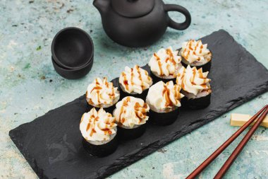 Suşi seti tepside, üstünde krem peynir ile servis edilir.