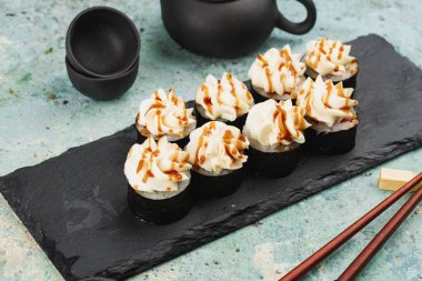 Suşi seti tepside, üstünde krem peynir ile servis edilir.