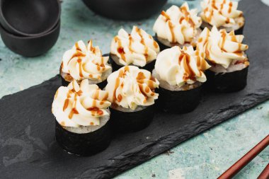 Suşi seti tepside, üstünde krem peynir ile servis edilir.