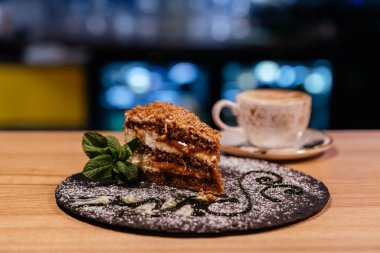 Çikolata katmanlı kremalı kek dilimi ve kahve fonda sıcak kahve fincanı.