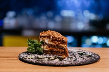 Çikolata katmanlı kremalı pasta dilimi ve siyah tabakta ince bir dal.