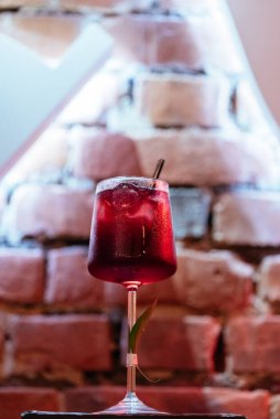 Ahududu ve alkol kokteyli. Tuğlaların arkasında buzlu cam var. 