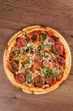 Ahşap masa arkasında sosis ve domatesli taze pişmiş lezzetli pizza.