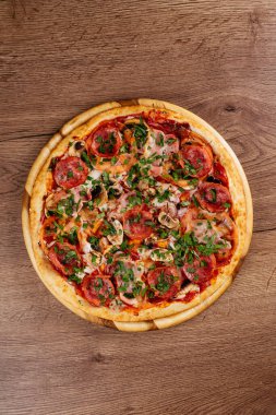 Ahşap masa arkasında sosis ve domatesli taze pişmiş lezzetli pizza.